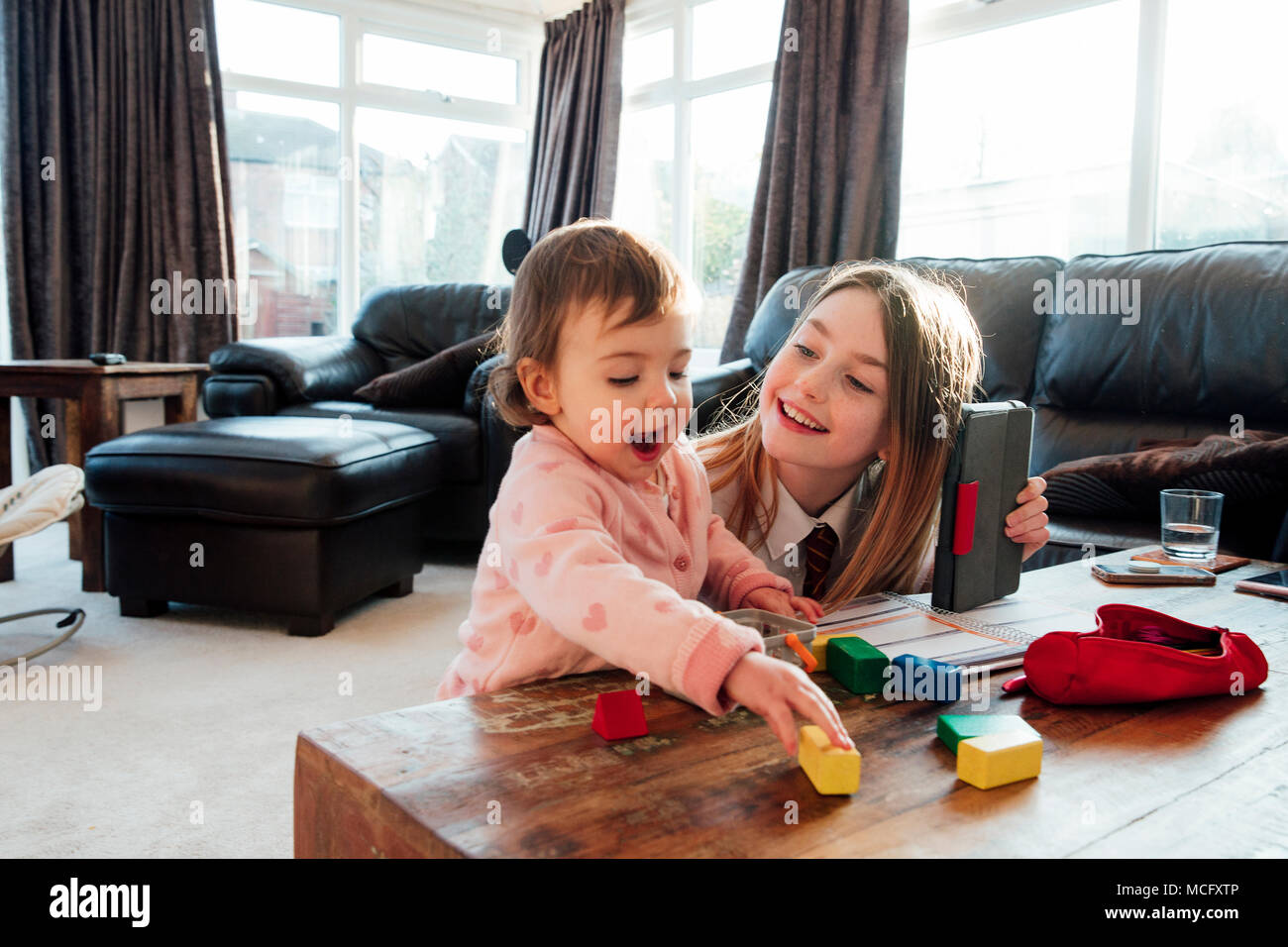 Bambina si distrae la sua sorella mentre lei sta cercando di studiare a casa. Stanno giocando con blocchi giocattolo insieme. Foto Stock