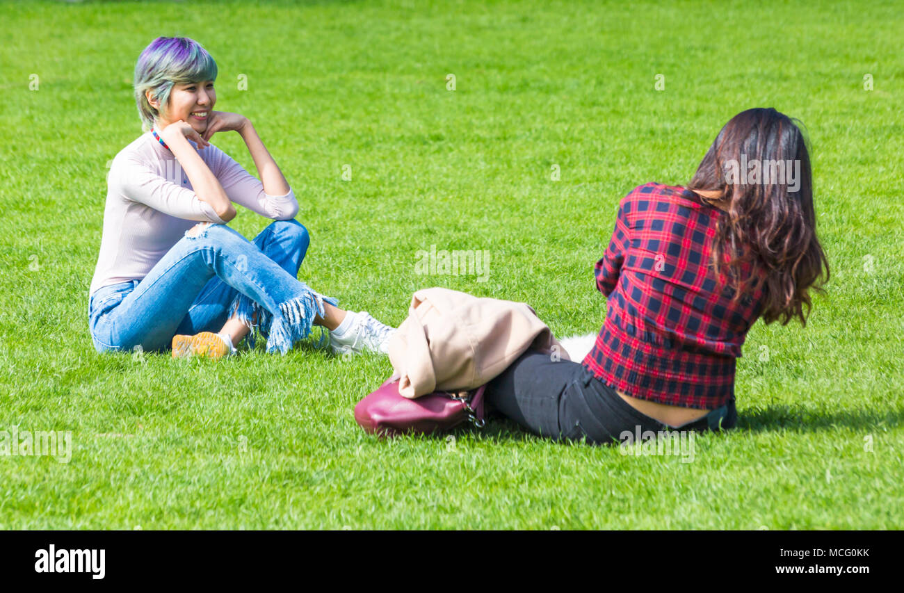 Due giovani donne seduta avendo divertimento sul prato del Royal Pavilion motivi, Brighton East Sussex, England Regno Unito nel mese di aprile Foto Stock