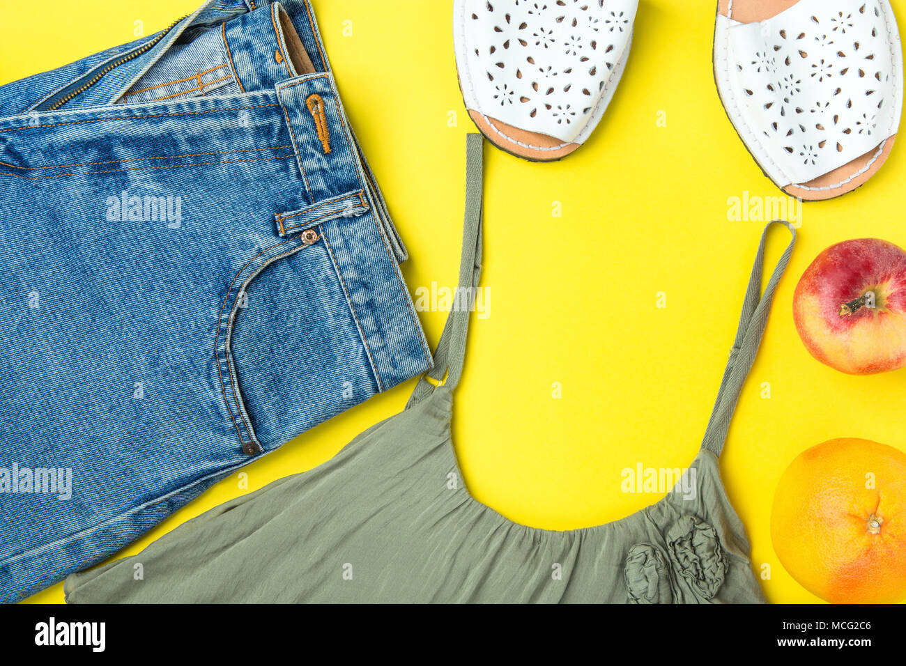 Classic donne Jeans Denim Shorts con frange di colore Oliva Tank Top Espandrille sandali di pompelmo Apple su sfondo giallo. Lay piatto. Street estate Foto Stock