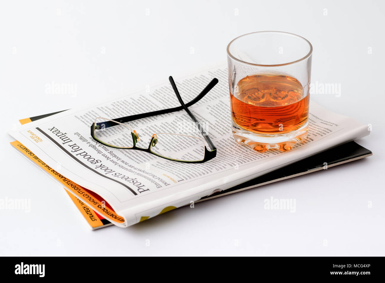 Gli occhiali da lettura e un bicchiere di whiskey su una rivista su investimenti finanziari, la pianificazione finanziaria, le negoziazioni di borsa. Sfondo bianco. Foto Stock