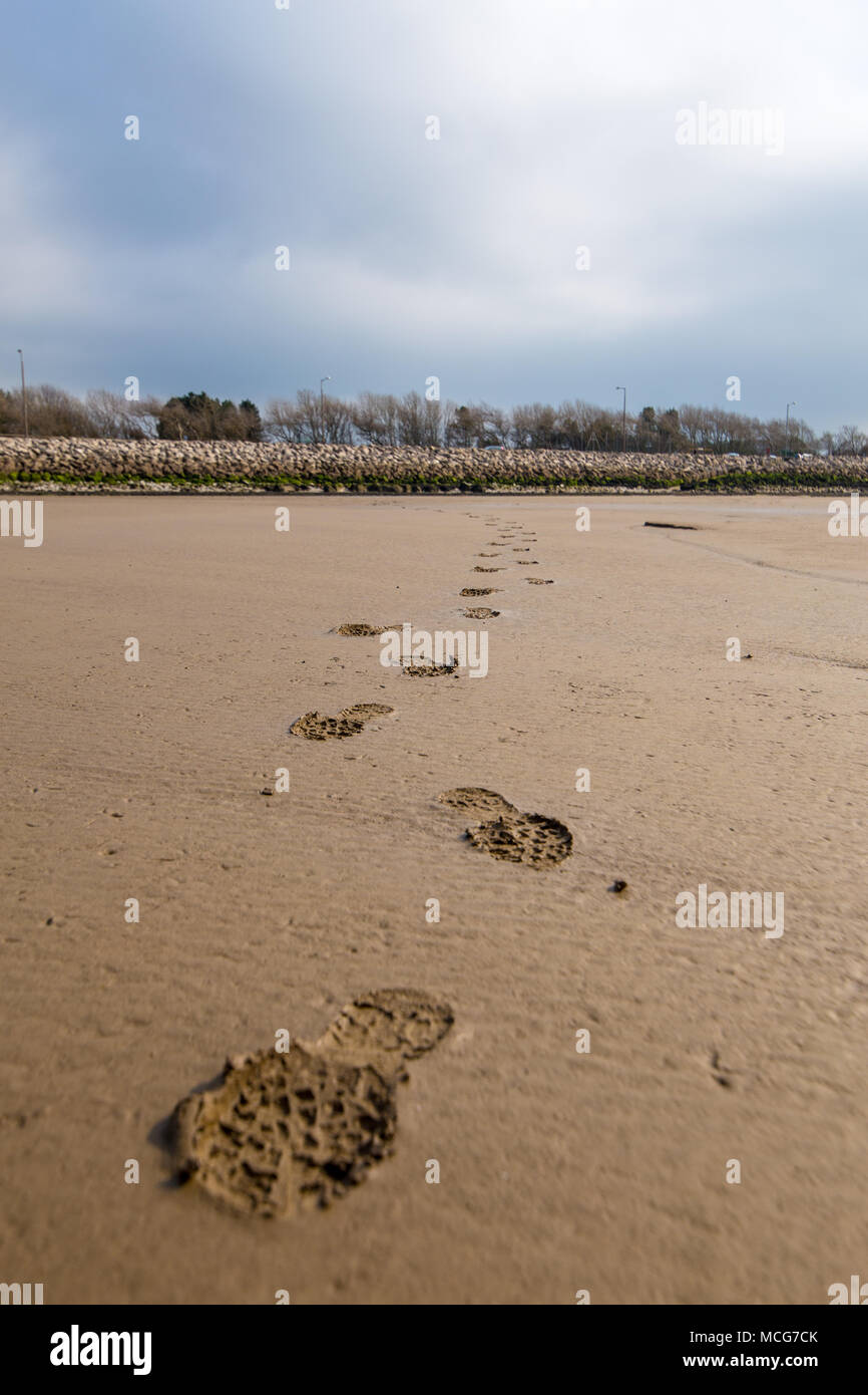 Una scia di impronte su un umido di spiaggia sabbiosa. Prese a Morecambe bay, Inghilterra, Regno Unito il 11 aprile 2018. Foto Stock