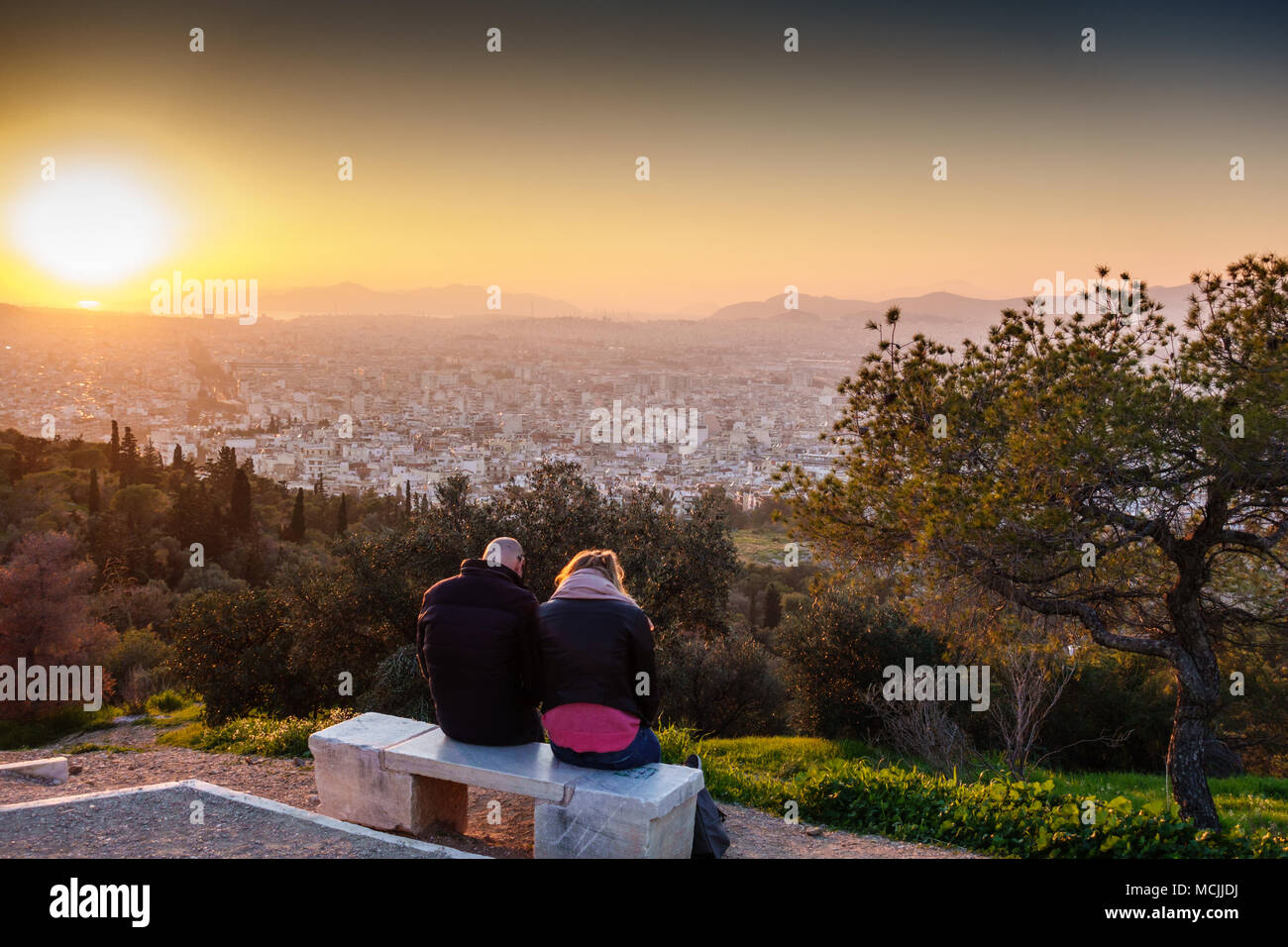 Vista posteriore di una coppia seduta su una panchina con la città di Atene a sfondo, Grecia Foto Stock