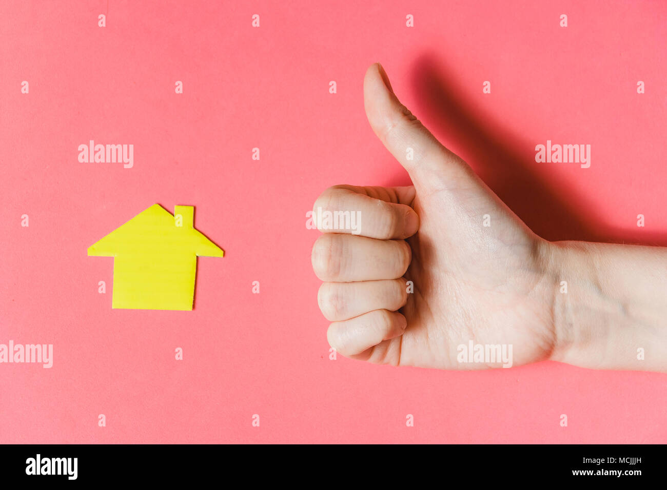Immobiliare di concetto. La mano che mostra i pollici fino a casa in miniatura su Backgroun rosa Foto Stock