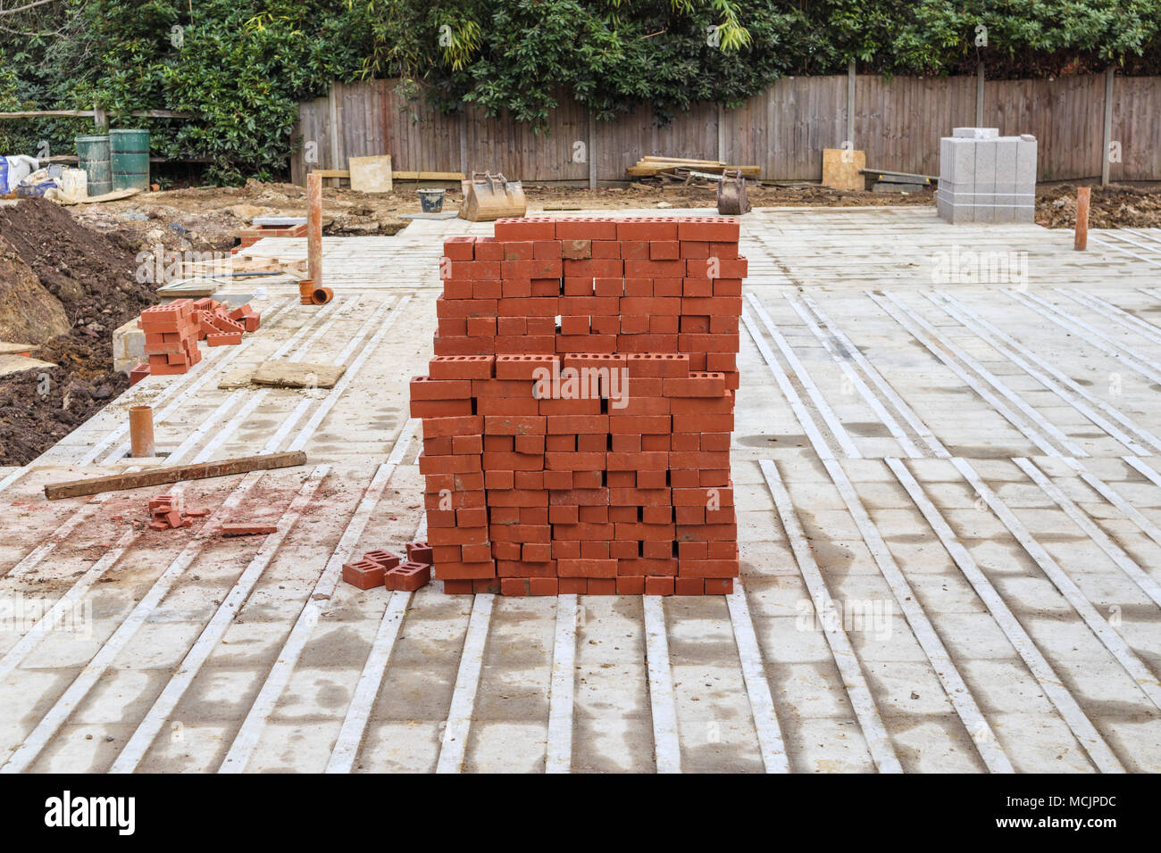Pila di tipica casa rossi mattoni impilati su un in parte costruito in alloggiamento nuovo materiale di riempimento o infill sviluppo sito in costruzione nel sud-est dell'Inghilterra, Surrey, Regno Unito Foto Stock