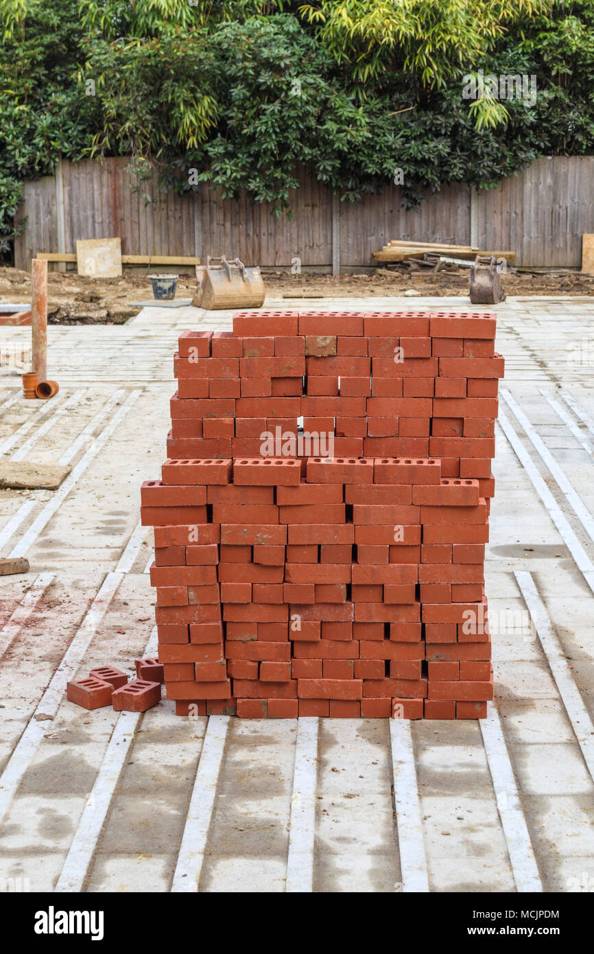 Pila di tipica casa rossi mattoni impilati su un in parte costruito in alloggiamento nuovo materiale di riempimento o infill sviluppo sito in costruzione nel sud-est dell'Inghilterra, Surrey, Regno Unito Foto Stock