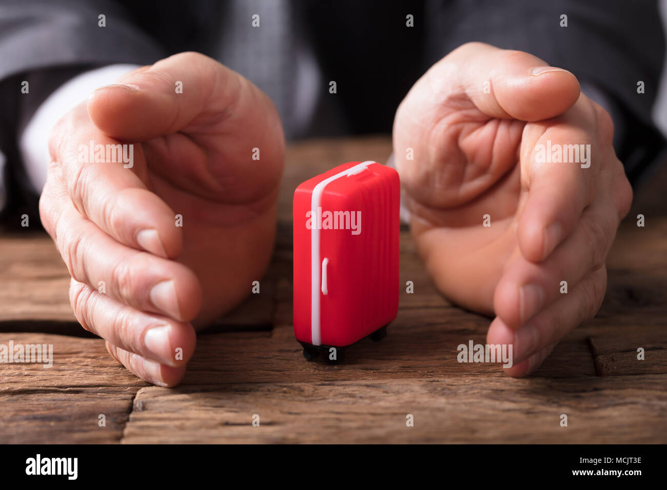 Close-up di un imprenditore la mano che tiene la valigia rossa sulla scrivania in legno Foto Stock