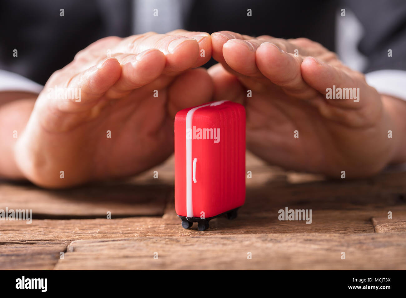 Close-up di un imprenditore la mano che tiene la valigia rossa sulla scrivania in legno Foto Stock