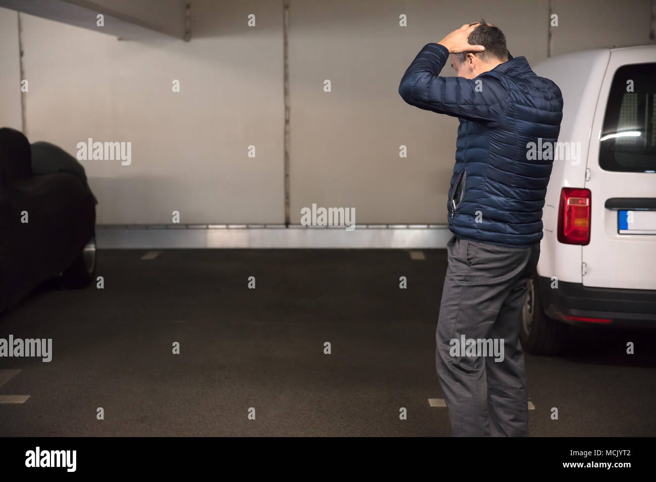 Vista posteriore di un scioccato uomo in piedi nel parcheggio dopo la sua auto è stata rubata Foto Stock