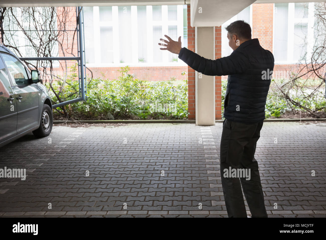 Vista posteriore di un scioccato uomo in piedi nel parcheggio dopo la sua auto è stata rubata Foto Stock
