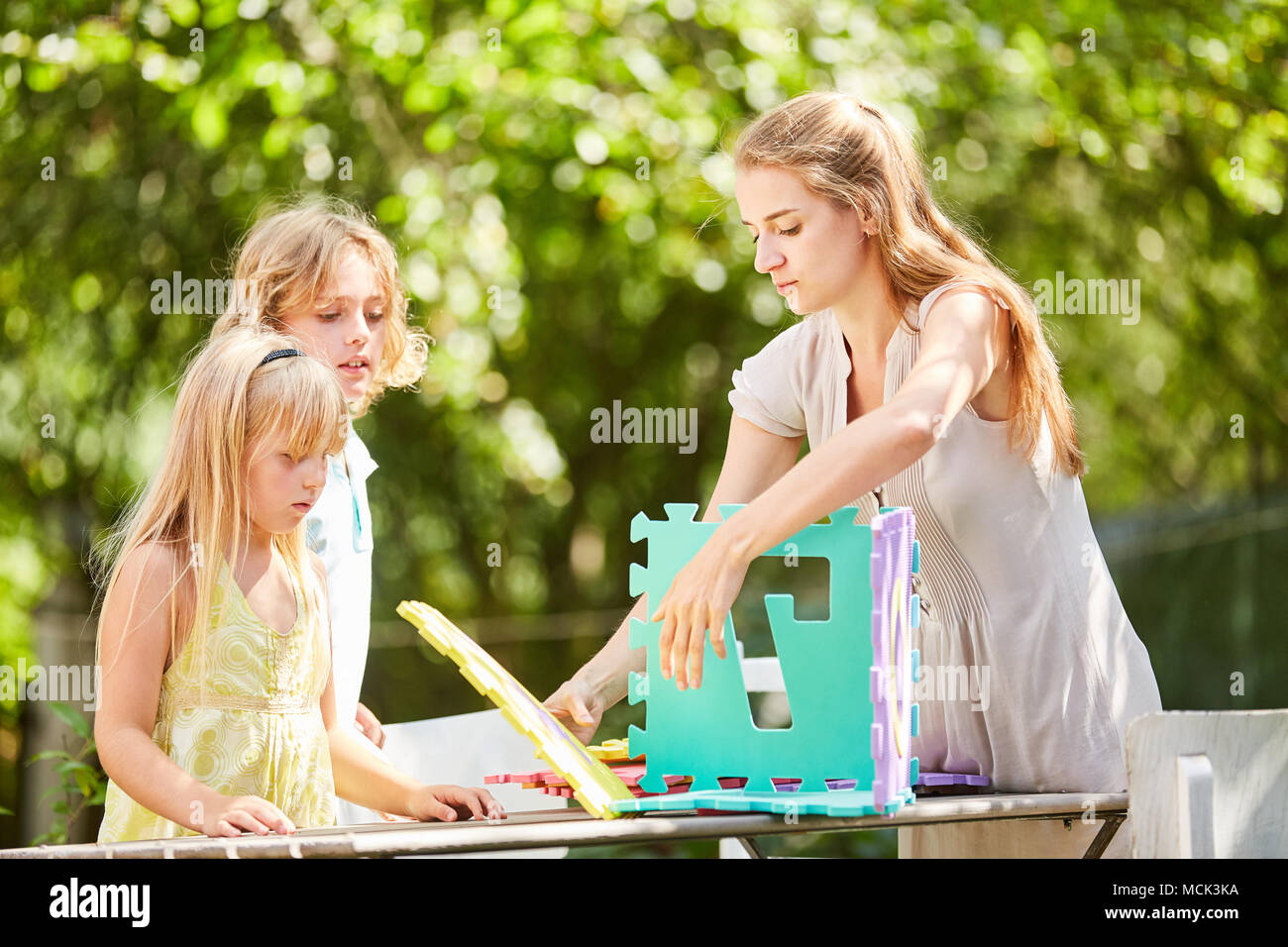Madre e bambini di giocare e di costruire un modello di casa con i pezzi del puzzle Foto Stock