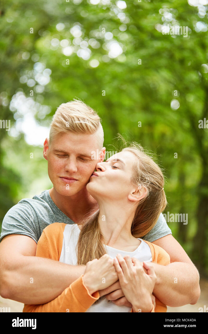 Giovane donna bacia il partner sulla guancia in estate in natura Foto Stock