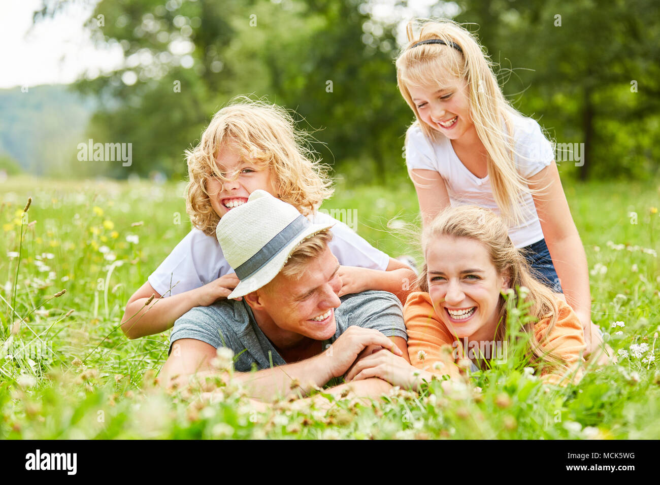 La famiglia e i bambini sono a ridere e giacente in erba nel giardino in primavera Foto Stock