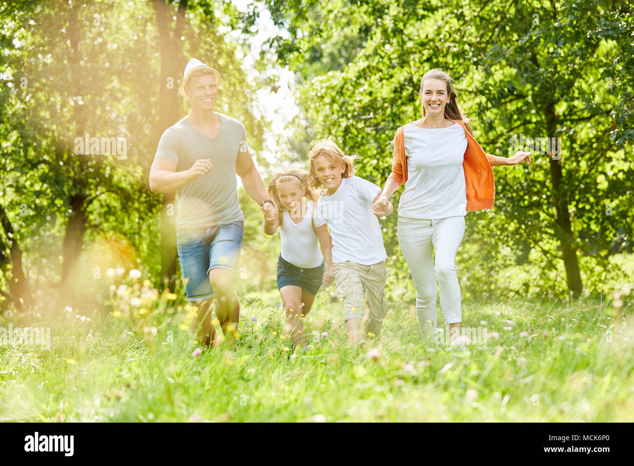 La famiglia felice e i ragazzi corrono insieme nel giardino in estate Foto Stock
