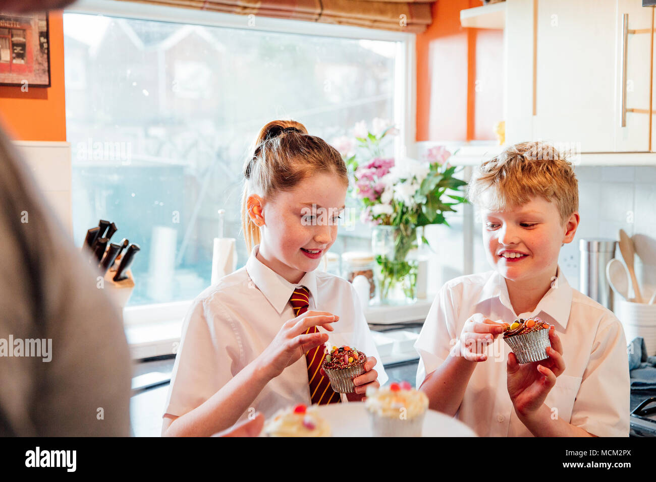 Due fratelli hanno venuto a casa dalla scuola e sono nella cucina di casa loro circa per mangiare i tortini. Foto Stock