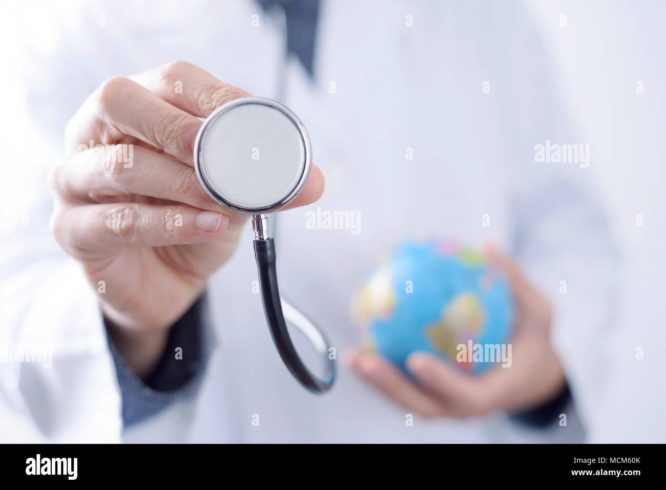 Primo piano di un giovane medico caucasica uomo con un globo mondo in una mano e uno stetoscopio nell'altra mano Foto Stock