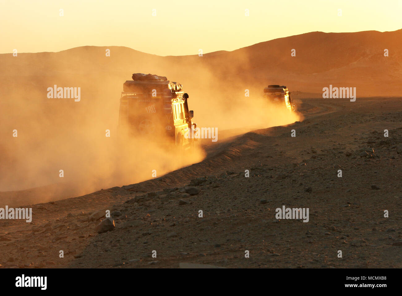 Un veicolo rende il suo modo attraverso le polverose strade rosso e vaste distese di nulla durante il tramonto nel nord del Sudan Foto Stock