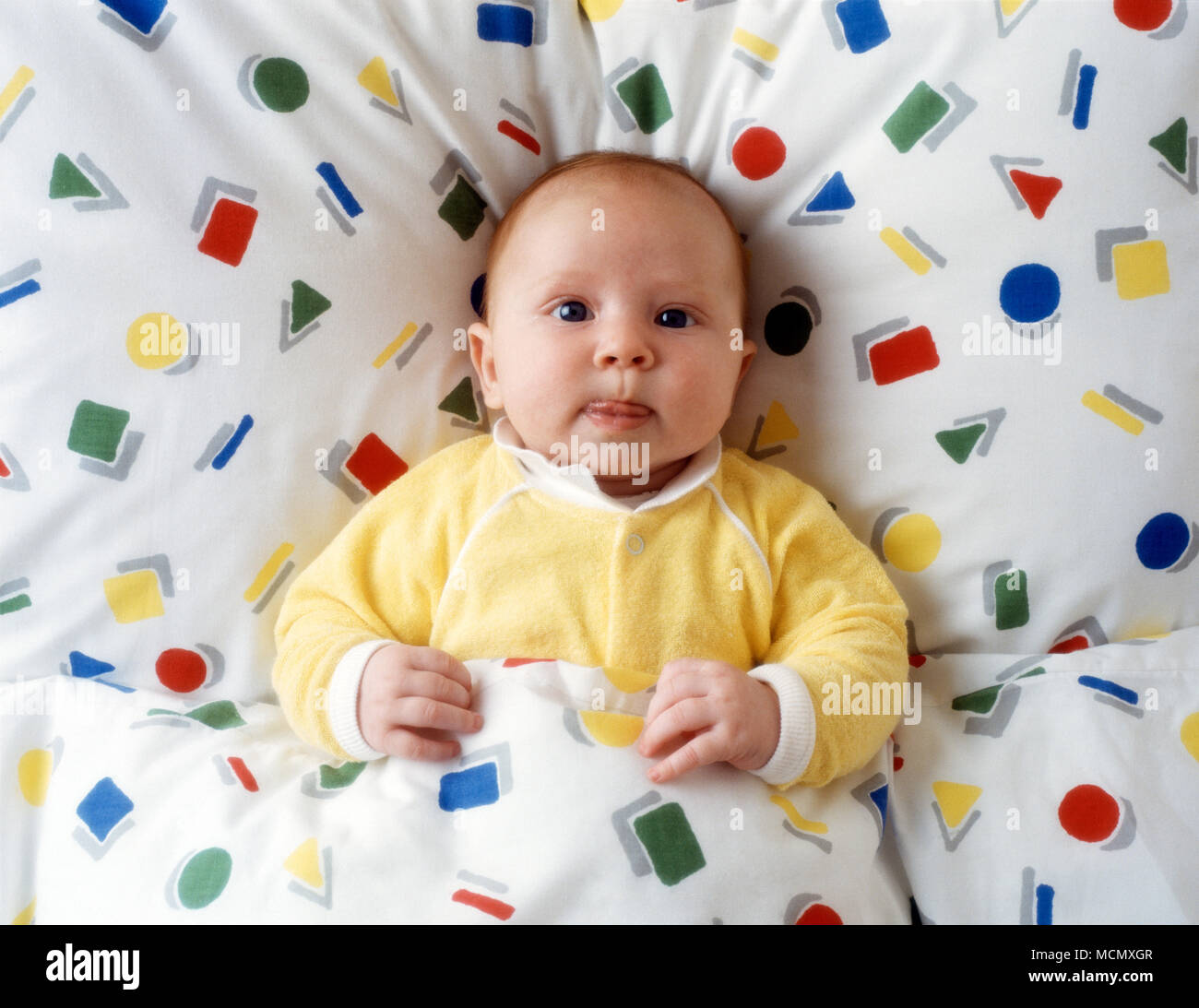 Bambino di sei mesi nel letto con piumone colorato Foto Stock