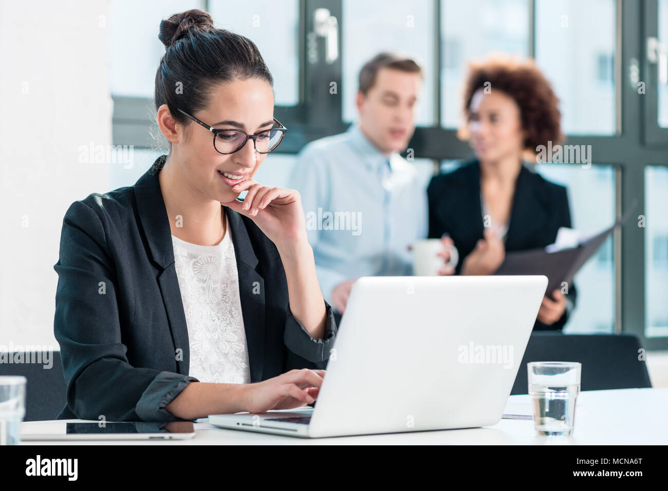 Giovane donna sorridente mentre si utilizza un portatile in ufficio Foto Stock