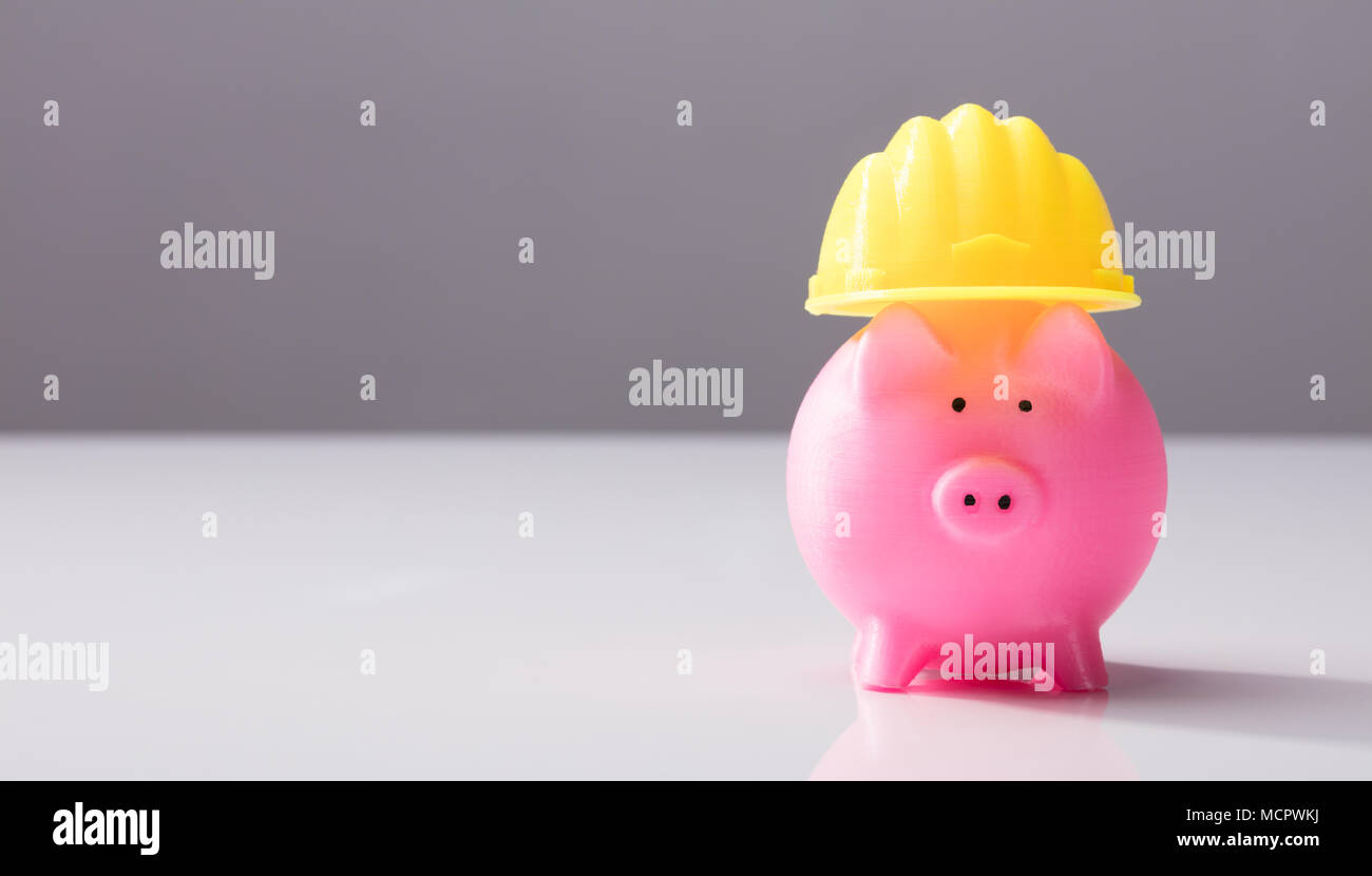 Close-up di un rosa Salvadanaio con Casco giallo sulla scrivania bianca Foto Stock