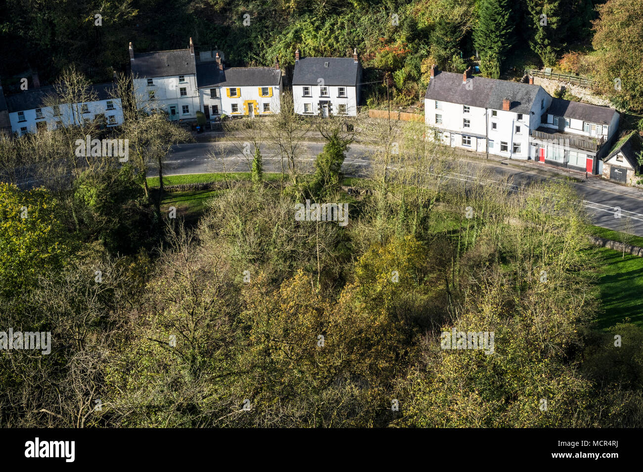 Guardando verso il basso sulle case e alberi illuminati da luce autunnale su una curva nella A6 road. Vista dall alto Tor, Matlock, Derbyshire, England, Regno Unito Foto Stock