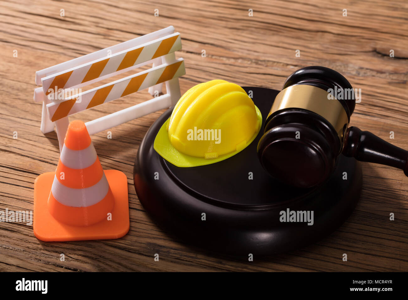 Martello con barriera stradale, elmetto e cono di traffico sulla scrivania in legno Foto Stock