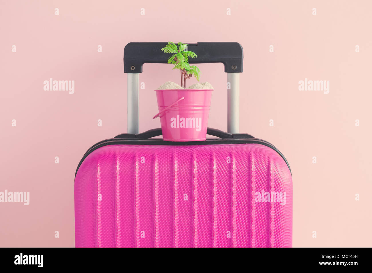 Valigia con piccolo secchio pieno di sabbia e Palm tree contro di rosa pastello minima di sfondo la vacanza estiva concetto creativo. Foto Stock
