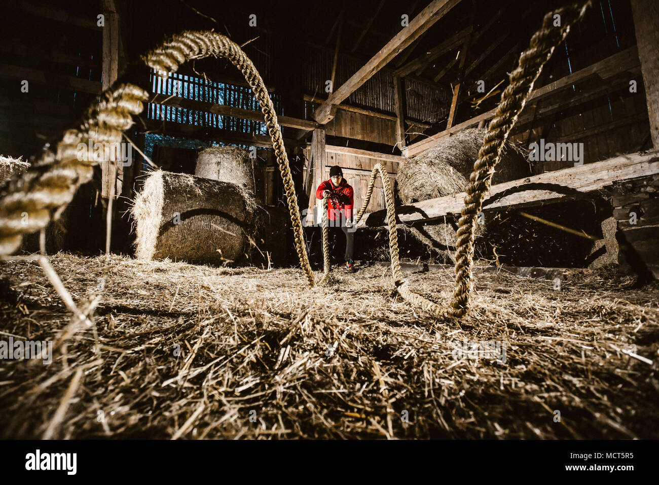 Crossfit atleta esercitando con funi di battaglia nel vecchio fienile Malopolskie, Polonia Foto Stock