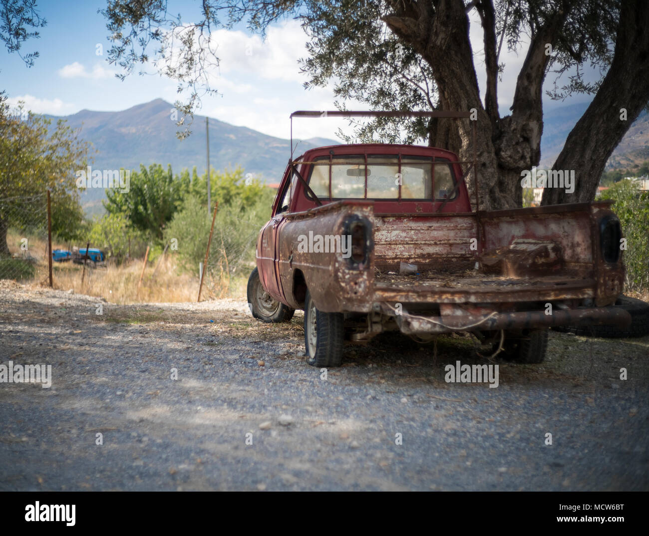 Rusty abbandonato auto sulla strada mediante una struttura ad albero Foto Stock