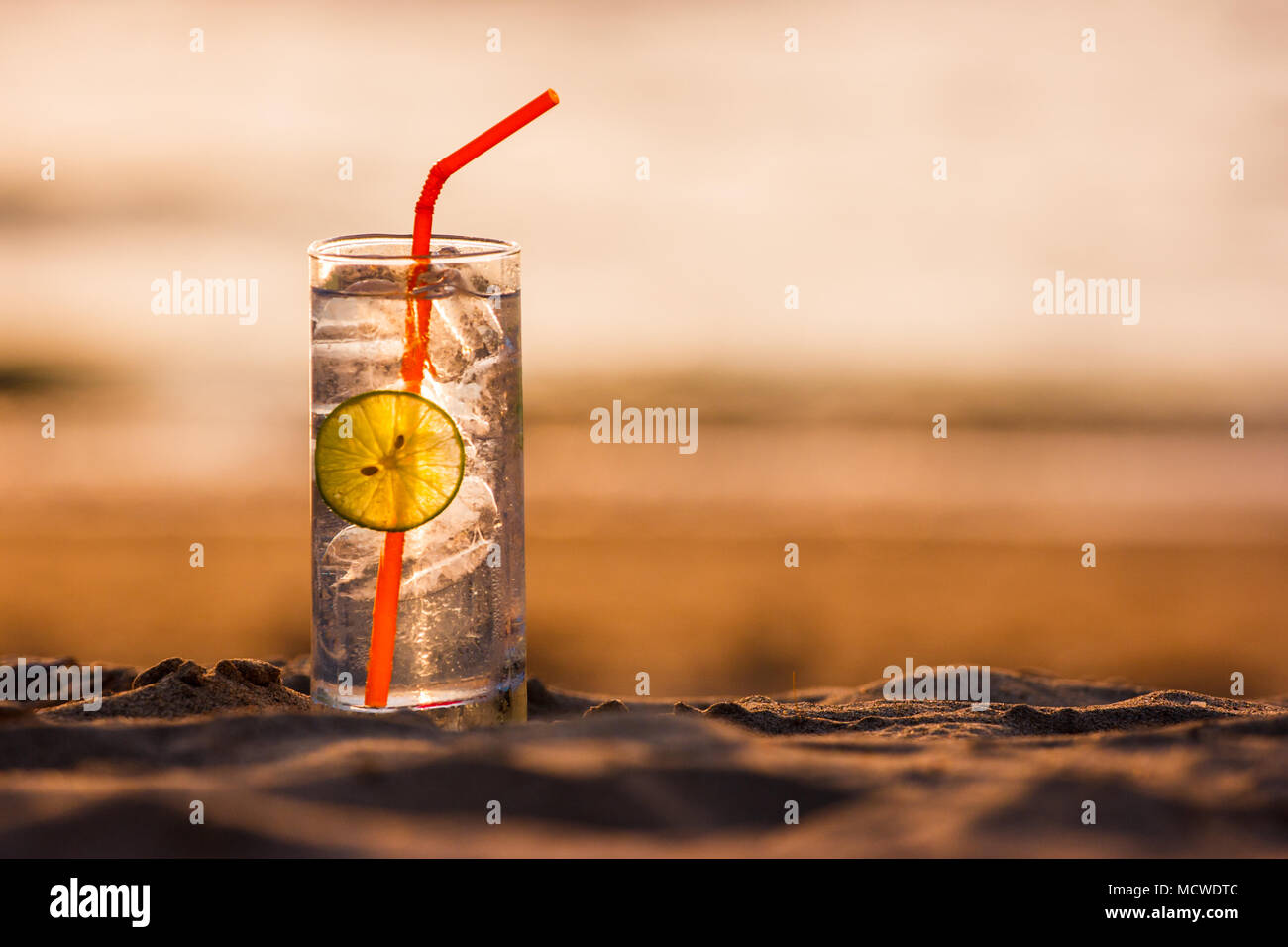 Immagine di un bicchiere di Gin Tonic con paglia e calce slice sulla spiaggia al tramonto. Long Beach, Ko Lanta, Thailandia. Foto Stock