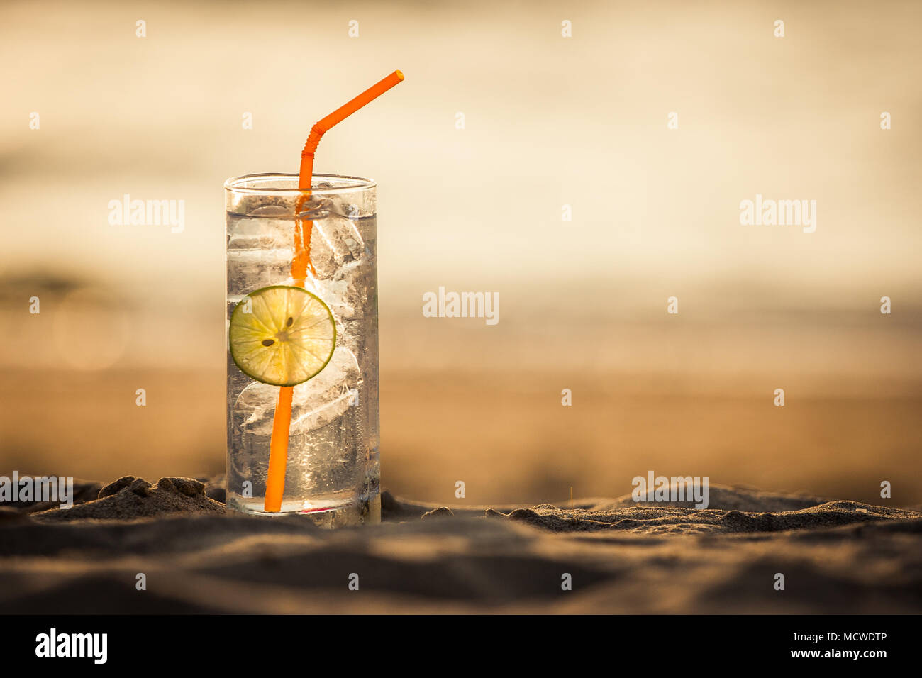 Immagine di un bicchiere di Gin Tonic con paglia e calce slice sulla spiaggia al tramonto. Long Beach, Ko Lanta, Thailandia. Foto Stock