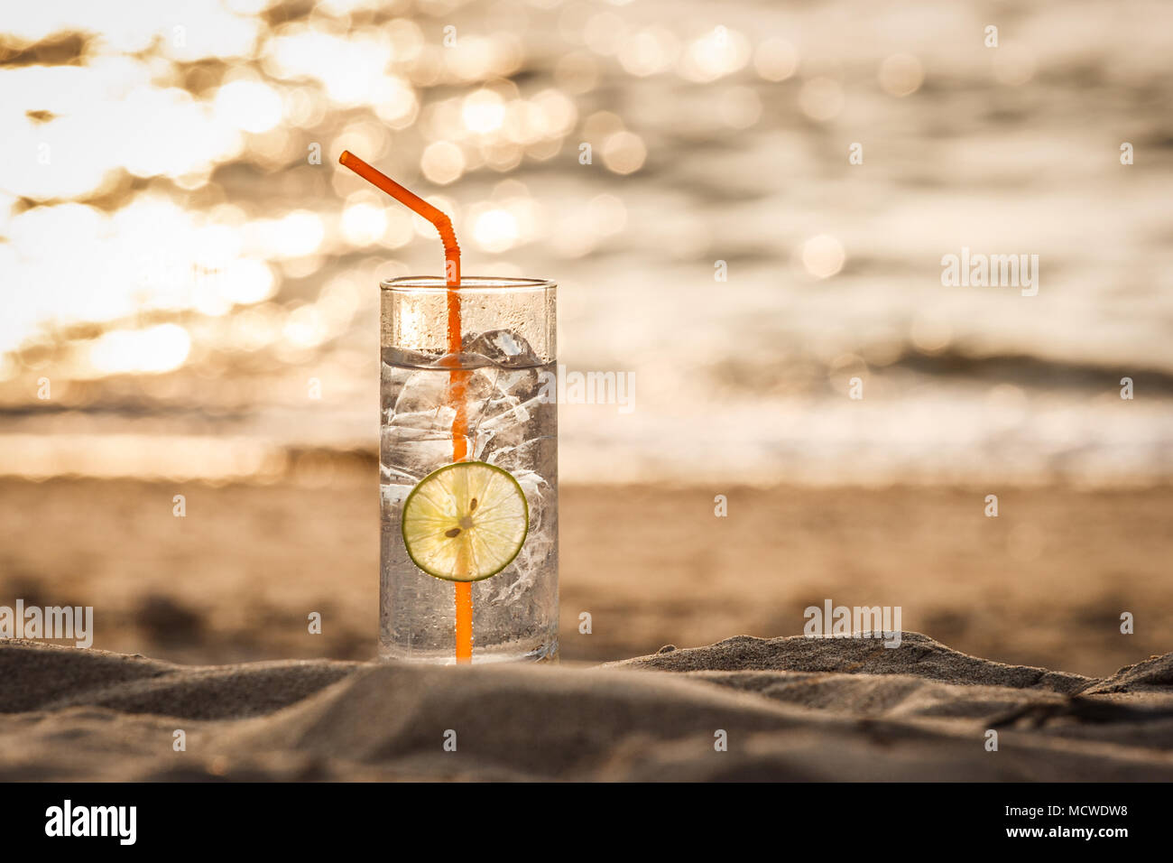 Immagine di un bicchiere di Gin Tonic con paglia e calce slice sulla spiaggia al tramonto. Long Beach, Ko Lanta, Thailandia. Foto Stock