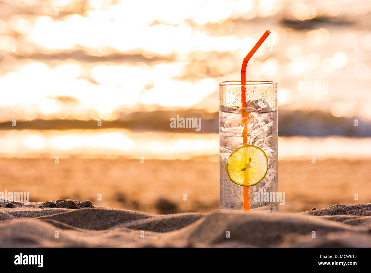 Immagine di un bicchiere di Gin Tonic con paglia e calce slice sulla spiaggia al tramonto. Long Beach, Ko Lanta, Thailandia. Foto Stock