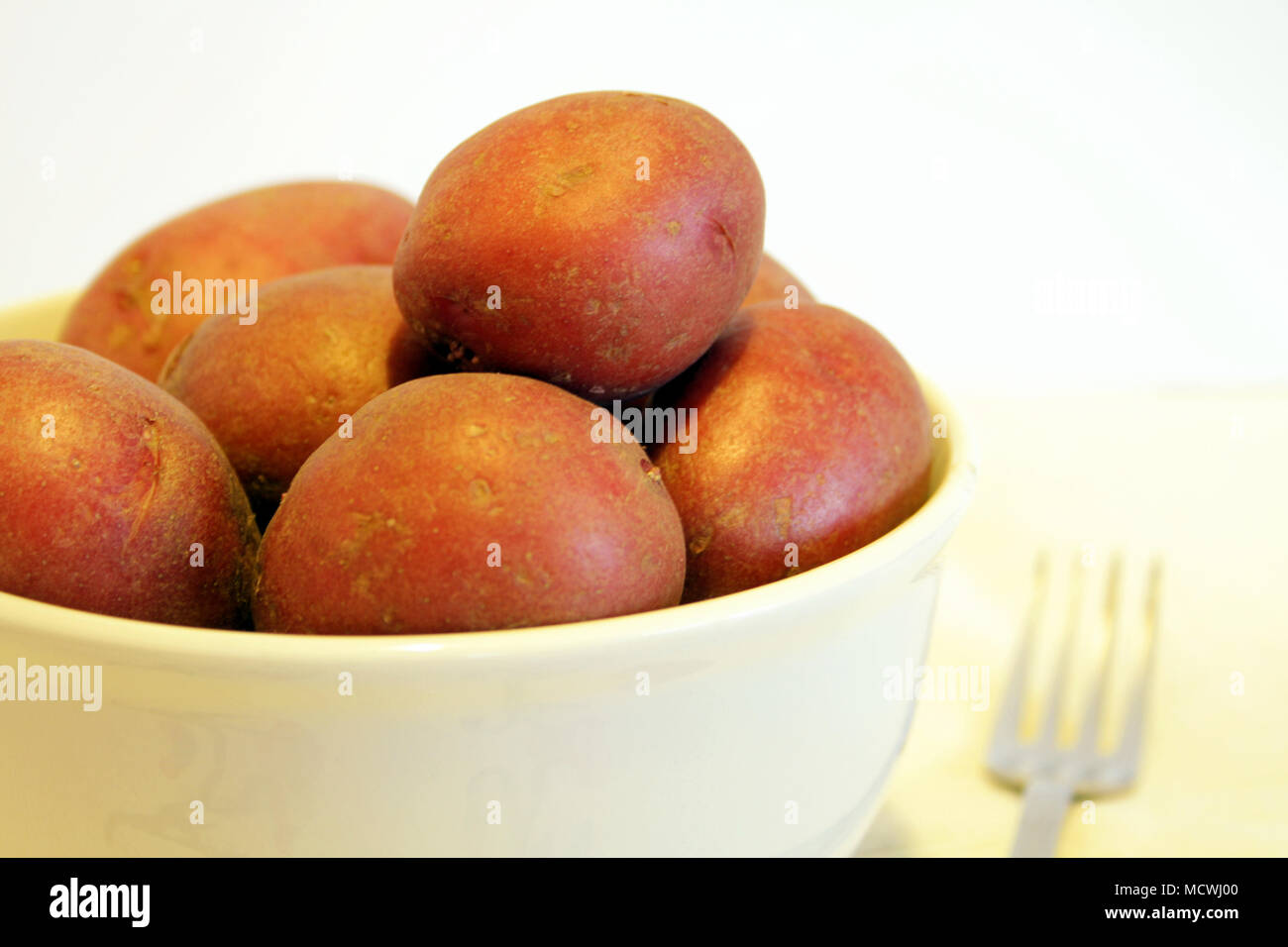 Una ciotola di patate novelle rosse si siede contro uno sfondo bianco con una forcella sfocata accanto ad essa. Foto Stock