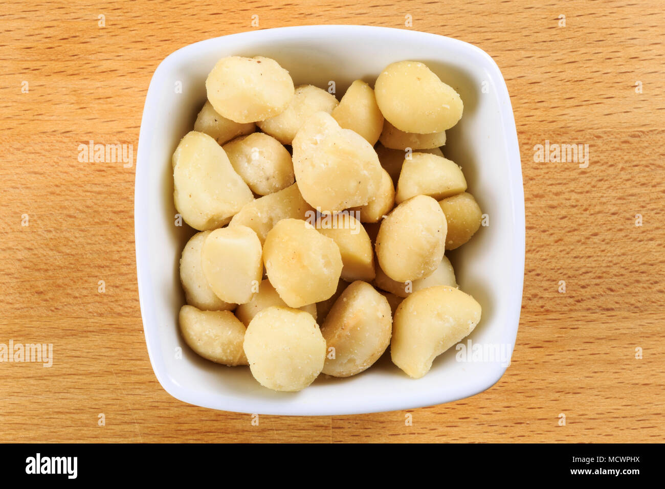 Colpo di overhead di materie di noci di macadamia in una ciotola bianco su una tavola di legno dello sfondo. Noci di Macadamia sono i semi della struttura ad albero di macadamia, Macadamia tetrap Foto Stock