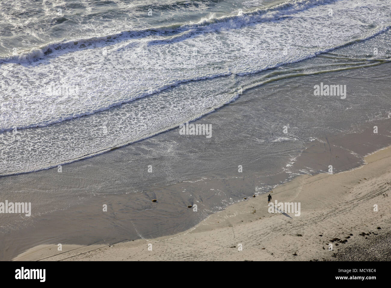 Un elevato overhead vista di una persona a piedi lungo la spiaggia con le onde in laminazione. Foto Stock