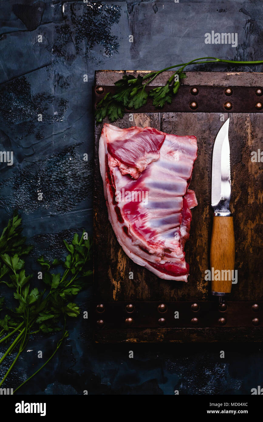 Vista superiore della carne di manzo crudo nervature sulla tavola di legno con il coltello sul buio superficie di cemento Foto Stock