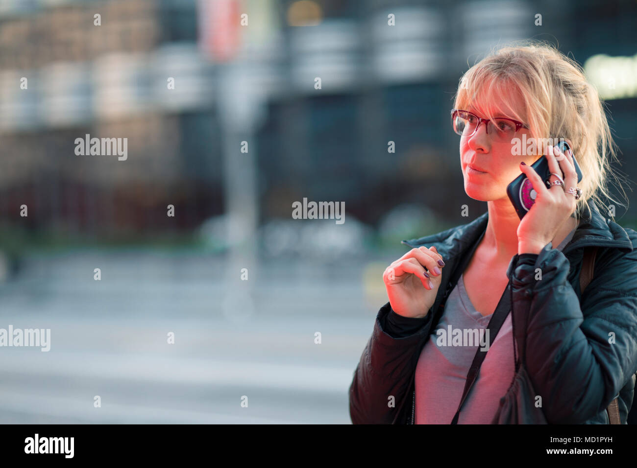 Bella ragazza parlando al telefono di notte su una strada trafficata cercando preplexed e stanca Foto Stock