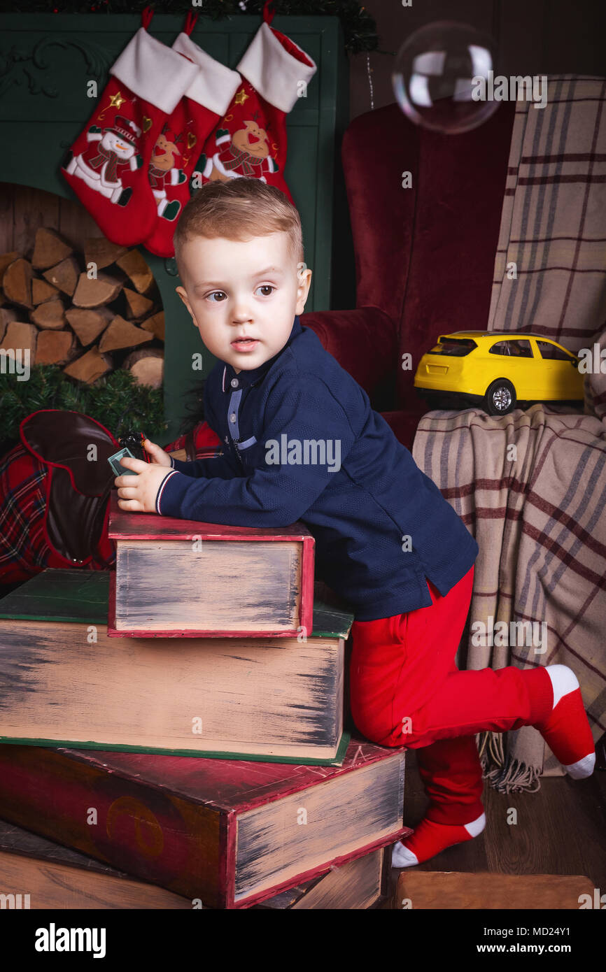 Un ragazzo in un blu scuro giacca e pantaloni rossi a Merry Christmas decorate rende un augurio di Santa Claus. Felice anno nuovo concetto di famiglia con il dono, plai Foto Stock