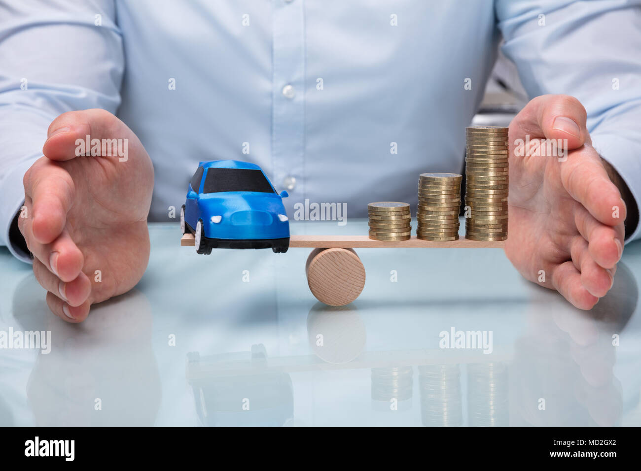 Commercianti la mano la protezione di equilibrio tra piccole auto blu e aumentando le monete impilate su altalena Foto Stock