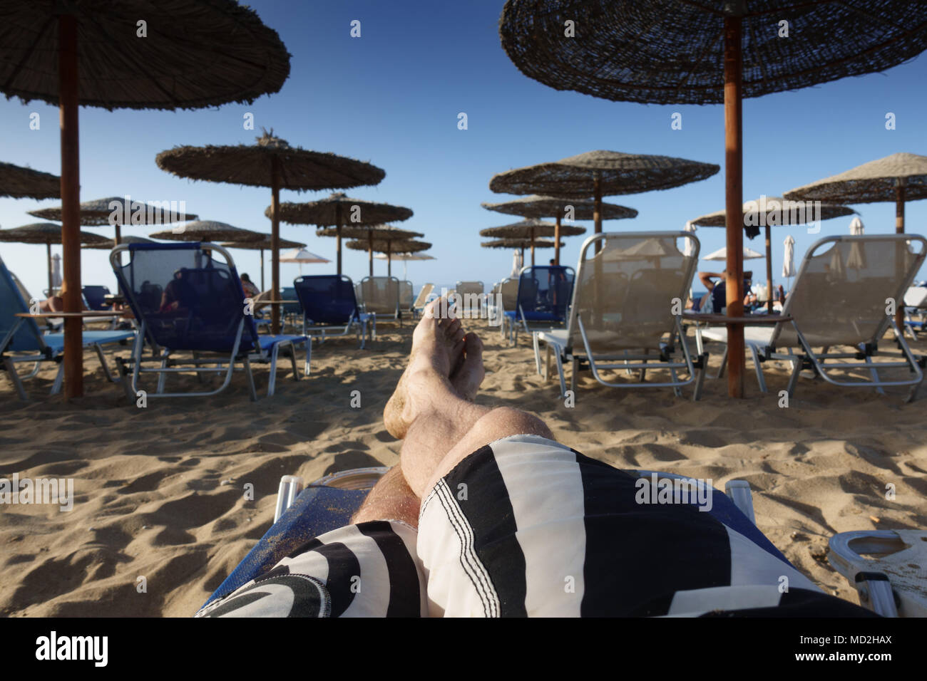 Sezione bassa di uomo a piedi nudi rilassante sulla spiaggia sabbiosa lounge chair Foto Stock