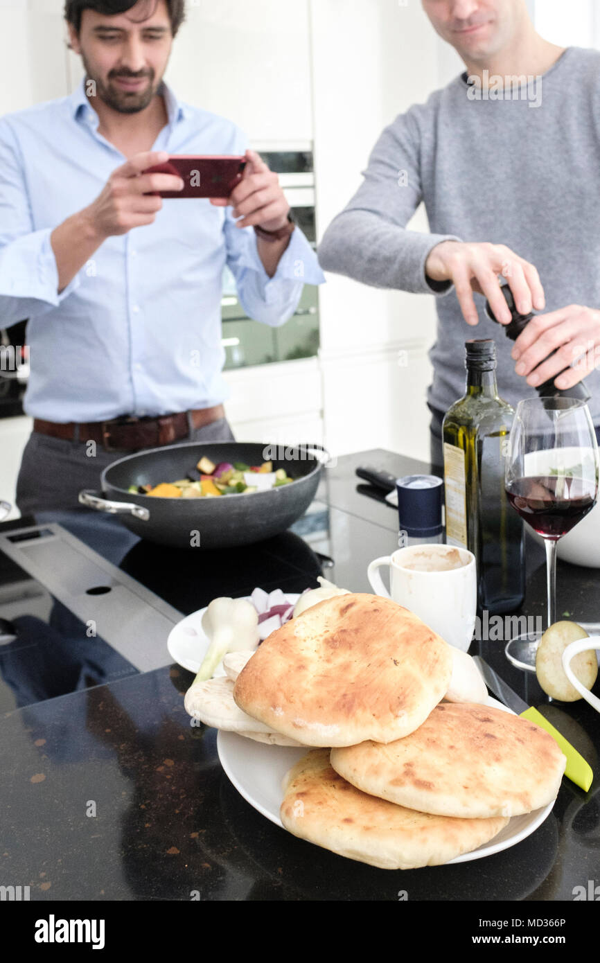 Uomo di scattare le foto del suo cibo sul suo telefono .amici cottura pasto vegetariano insieme. Foto Stock