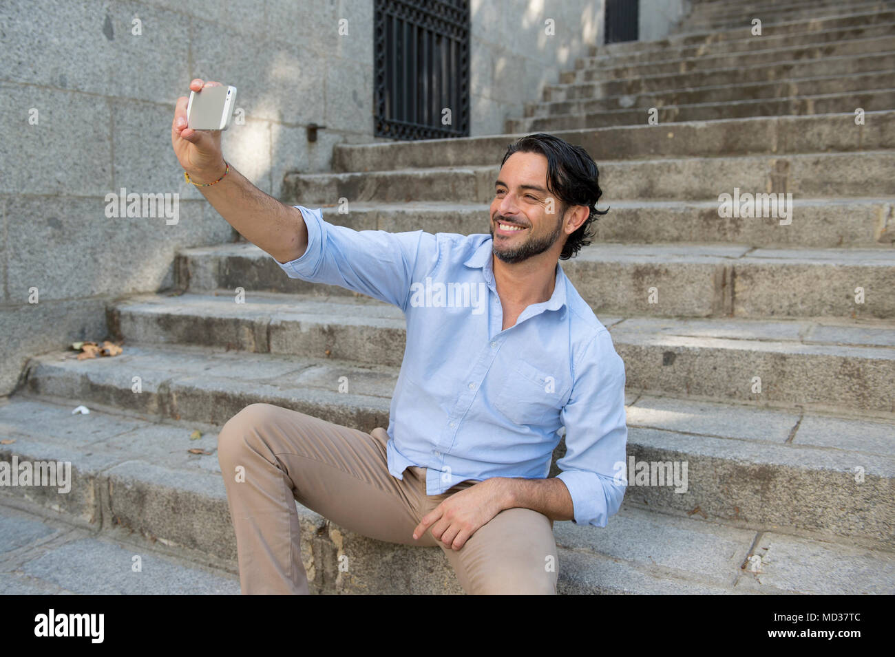 Giovani attraenti uomo latino sulla scalinata della città prendendo selfie picture divertirsi sul telefono cellulare seduti sulla scalinata in rete la tecnologia di comunicazione Foto Stock