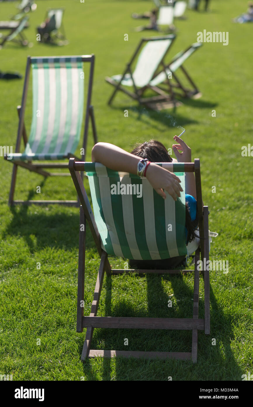 Londra, Regno Unito. Il 18 aprile 2018. Una donna che fuma una sigaretta seduto su una sedia a sdraio durante la calda primavera meteo in St James Park su un giorno quando la temperatura ha raggiunto 25 gradi a Londra. Foto data: mercoledì 18 aprile, 2018. Foto: Roger Garfield/Alamy Live News Foto Stock