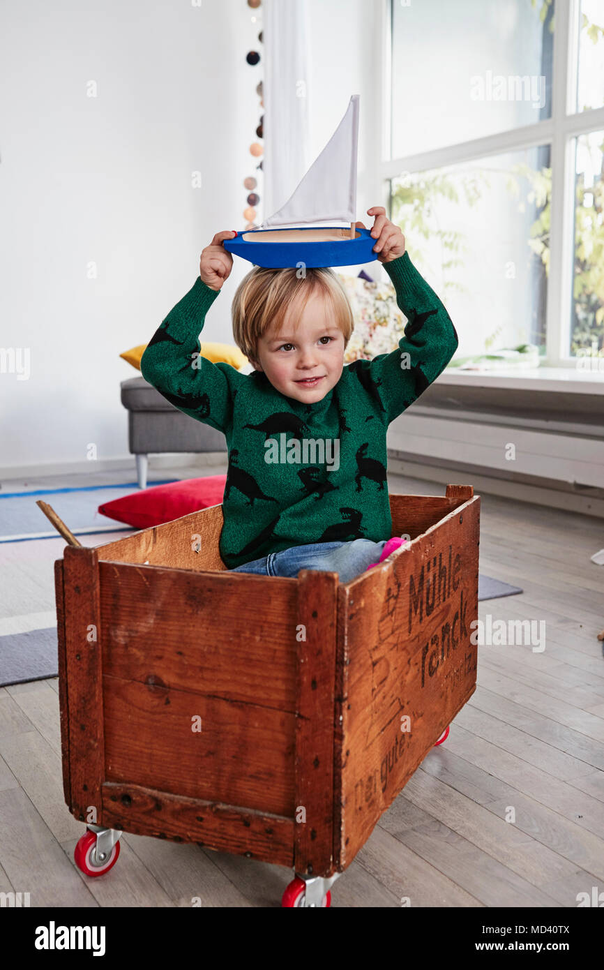 Ragazzo seduto in Toy Box, azienda barca giocattolo sulla testa Foto Stock