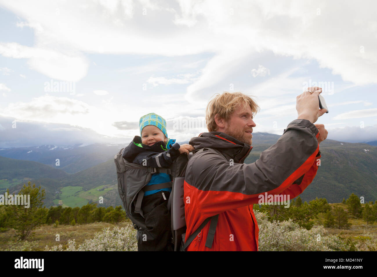 Escursionista maschio con figlio di fotografare il paesaggio di montagna, parco nazionale di Jotunheimen, Lom, Oppland, Norvegia Foto Stock