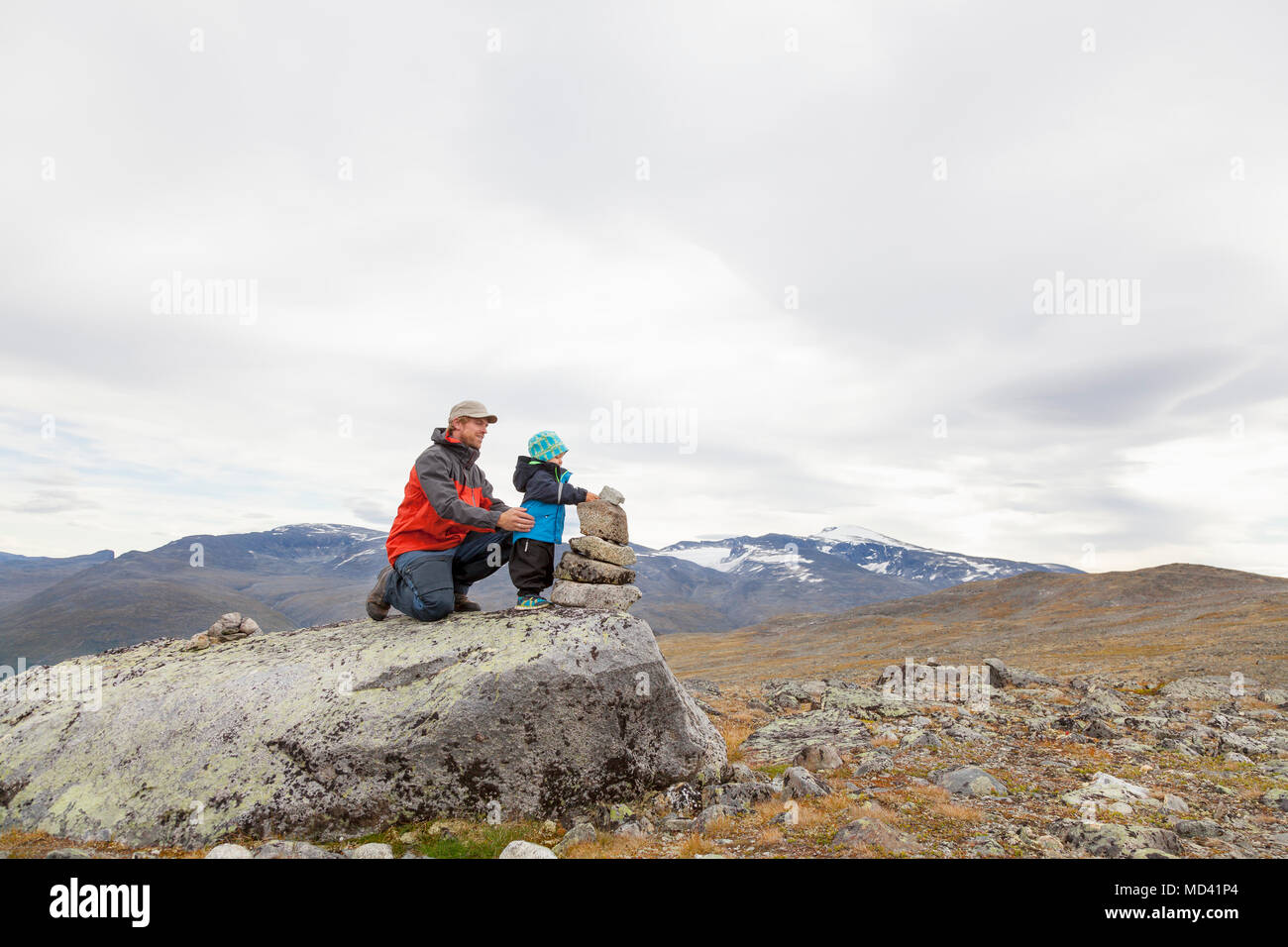 Escursionista maschio con figlio edificio cairn nel paesaggio di montagna, parco nazionale di Jotunheimen, Lom, Oppland, Norvegia Foto Stock