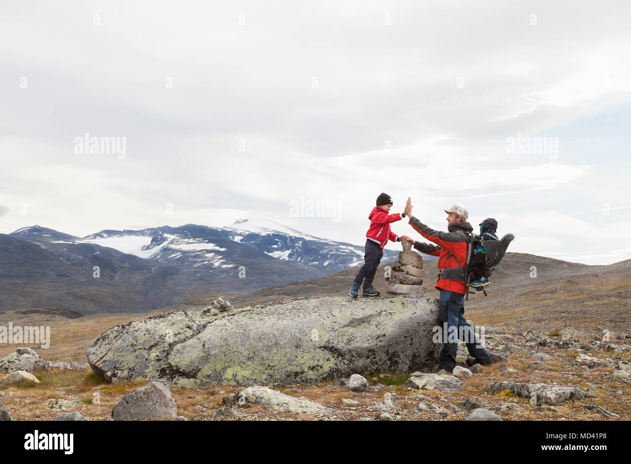 Uomo con figli alta fiving su cairn nel paesaggio di montagna, parco nazionale di Jotunheimen, Lom, Oppland, Norvegia Foto Stock