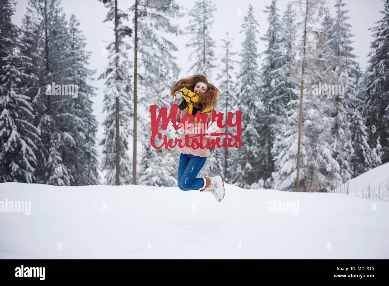 Giovane donna salta con buon Natale parole nella neve Foto Stock