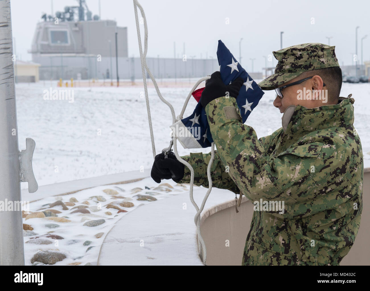 180320-N-BK DEVESELU435-0004, Romania (20 marzo 2018) Senior Chief specialista culinaria Jojo Caballero, assegnato al supporto navale Facility Deveselu, solleva il ensign per mattina colori nella neve. NSF Deveselu AAMDS e Romania sono co-localizzato con il rumeno 99th Base Militare e gioca un ruolo chiave nel missile balistico di difesa in Europa orientale. (U.S. Foto di Marina di Massa lo specialista di comunicazione 1a classe Jeremy Starr/rilasciato) Foto Stock