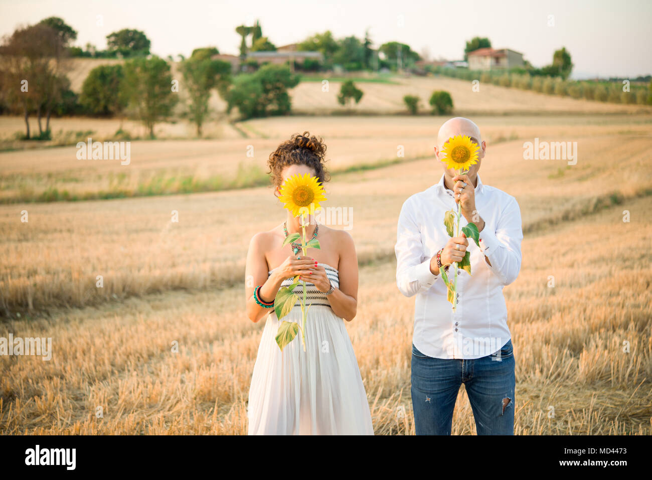 Coppia eterosessuale in un campo di girasoli di contenimento nella parte anteriore delle facce Foto Stock